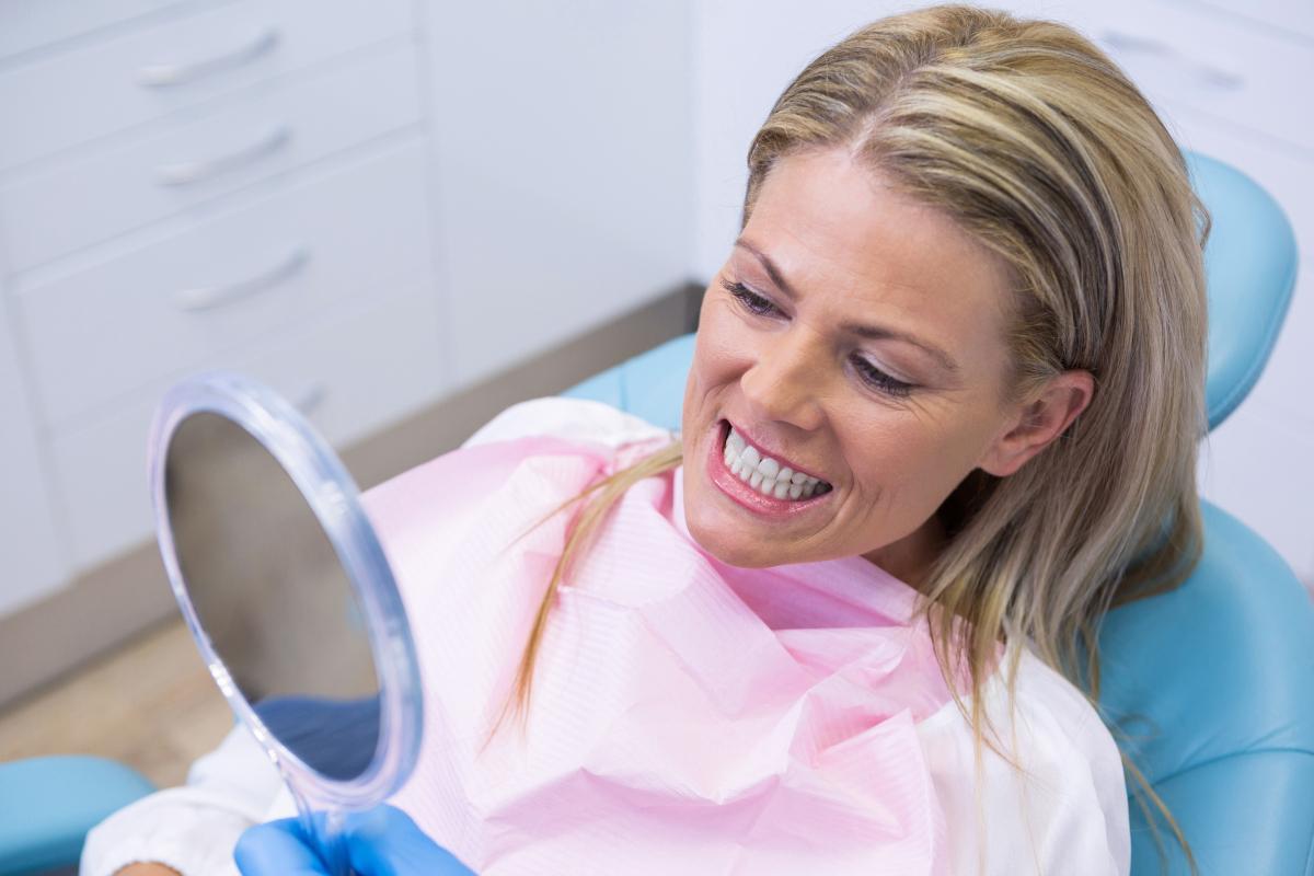 Woman in dental chair examining her smile in mirror at dental office
