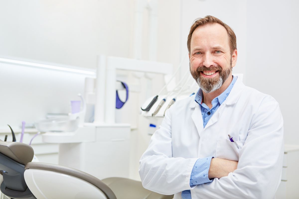 When to Call a Periodontist Male dentist in white coat smiling in modern dental office treatment room